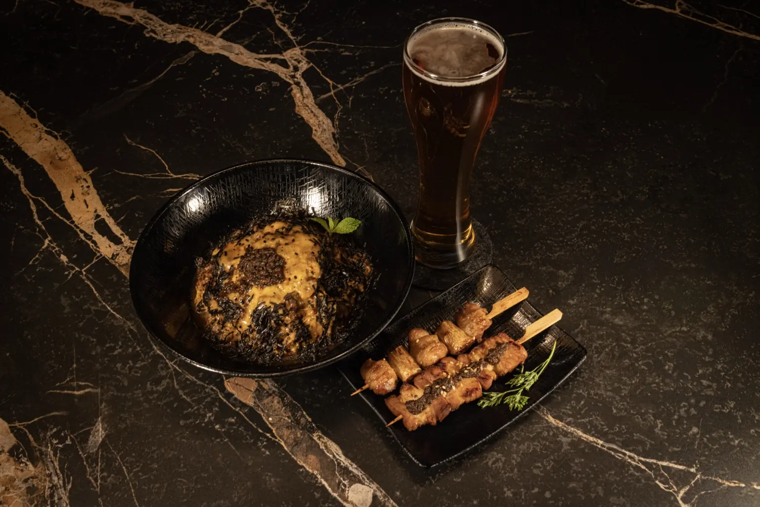 A Hotferno rice bowl, skewers, and beer on a black marble table